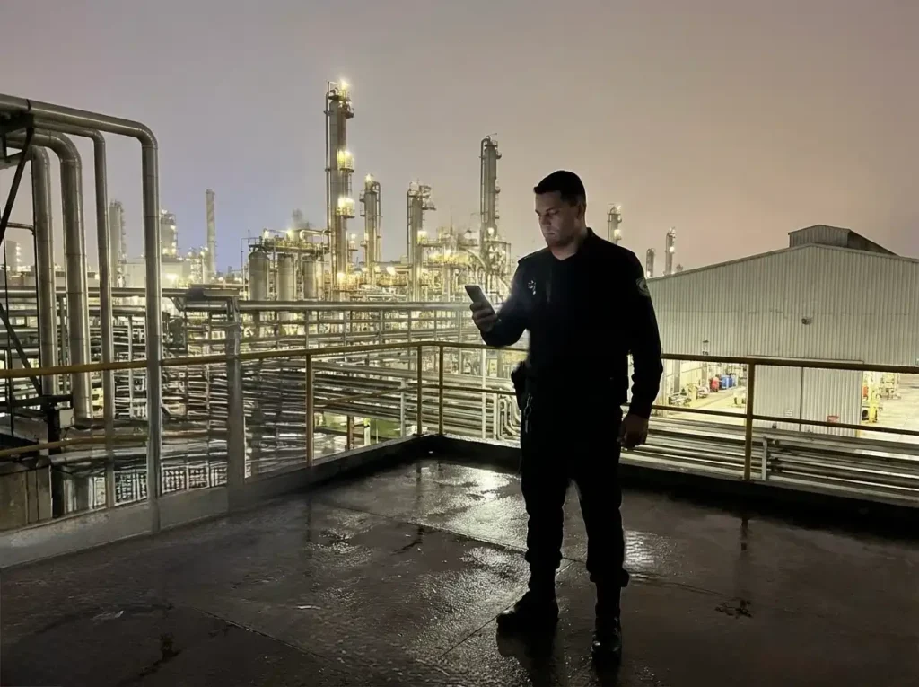 Vigilante em ronda noturna em instalação industrial utilizando sistema de monitoramento móvel.